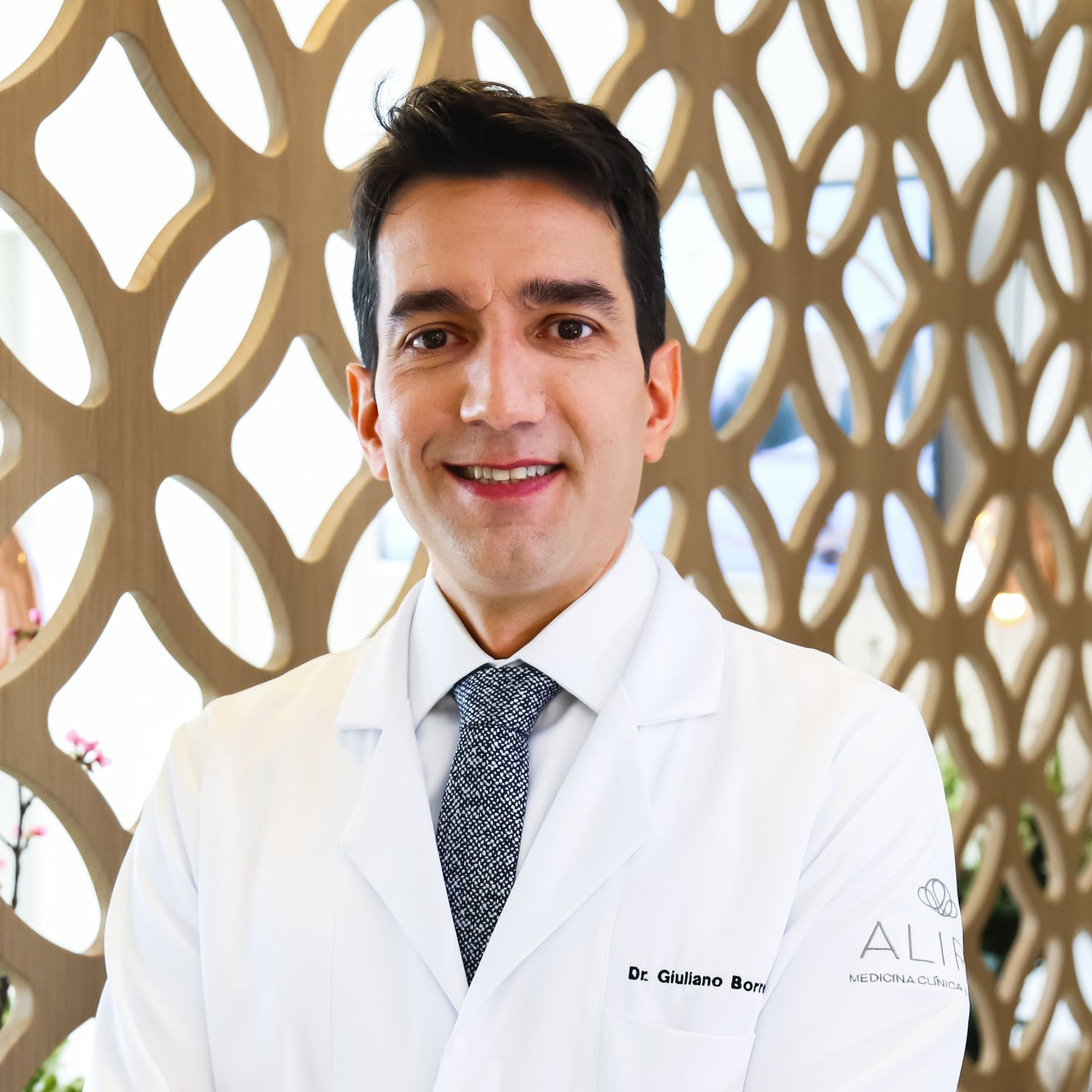 Um homem de jaleco branco e gravata está sorrindo para a câmera