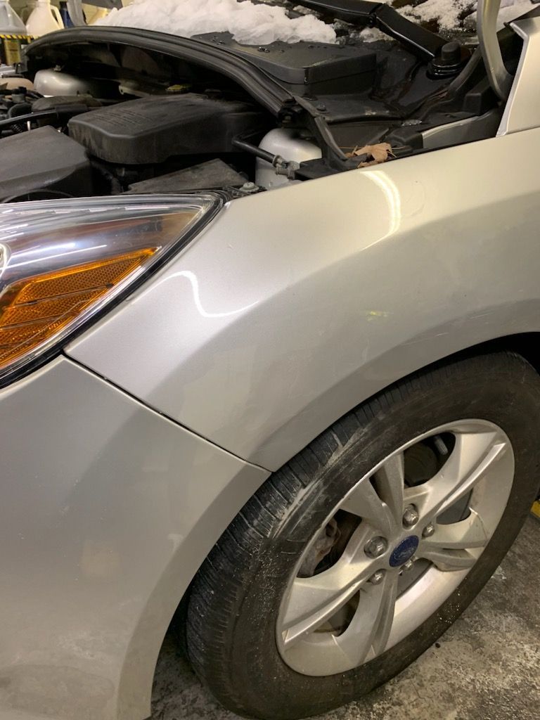 A silver car with the hood up is parked in a garage.