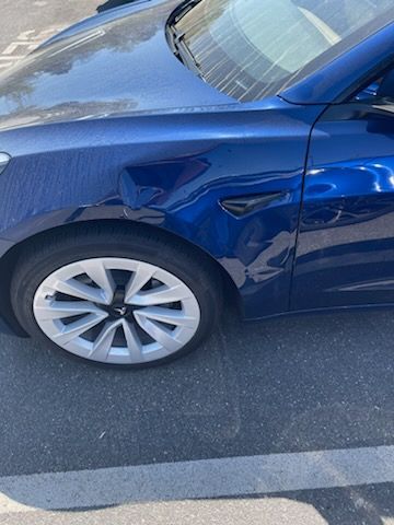 A blue tesla model 3 is parked in a parking lot.