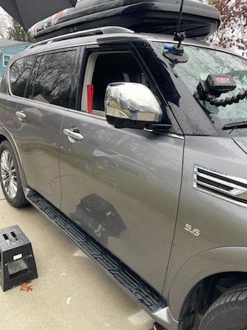 A gray suv with a roof box on top of it is parked in a driveway.