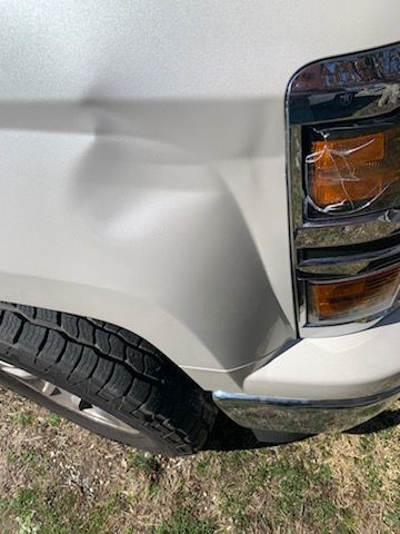 A white truck with a damaged bumper is parked in the grass.