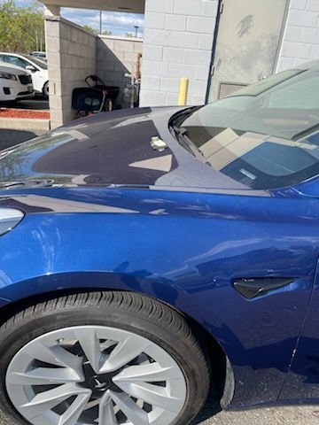 A blue tesla model 3 is parked in a parking lot.