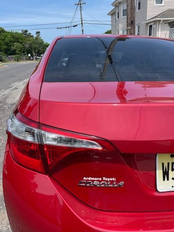 A red toyota corolla is parked on the side of the road.