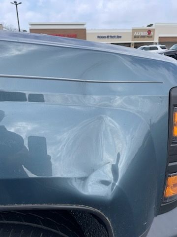 A close up of a truck 's fender with a dent in it.