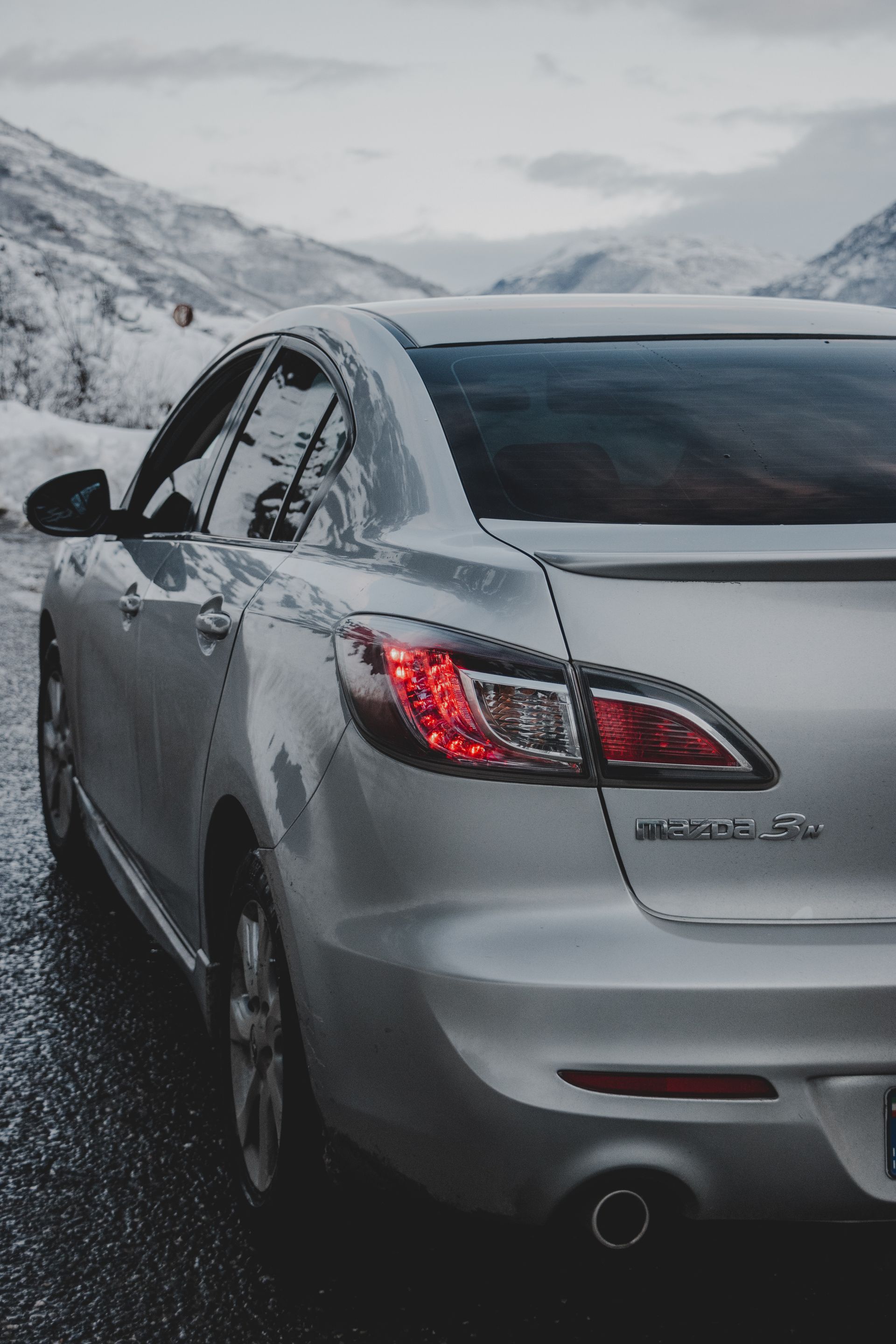 Rear view of a silver Mazda 3 on a snowy road.