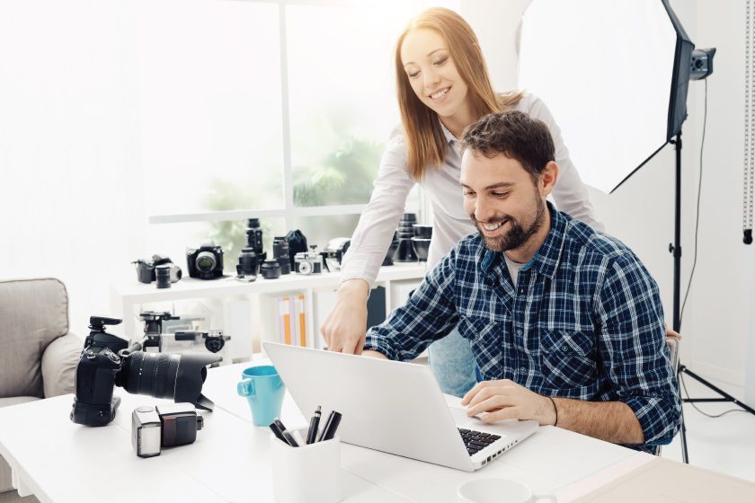 Un homme et une femme dans un studio entouré de caméras regardent un ordinateur portable