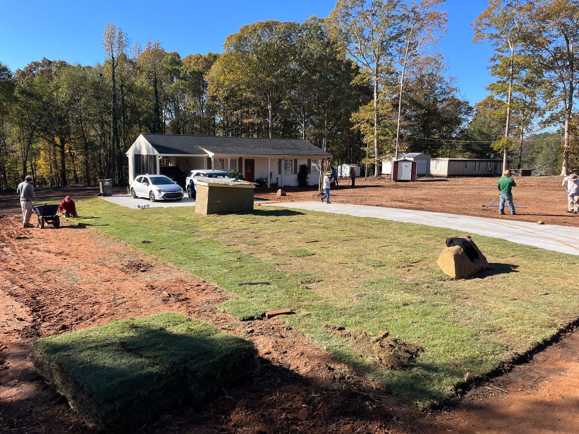 A trench dug in red soil, with black corrugated pipe for drainage, next to a building and lawn.