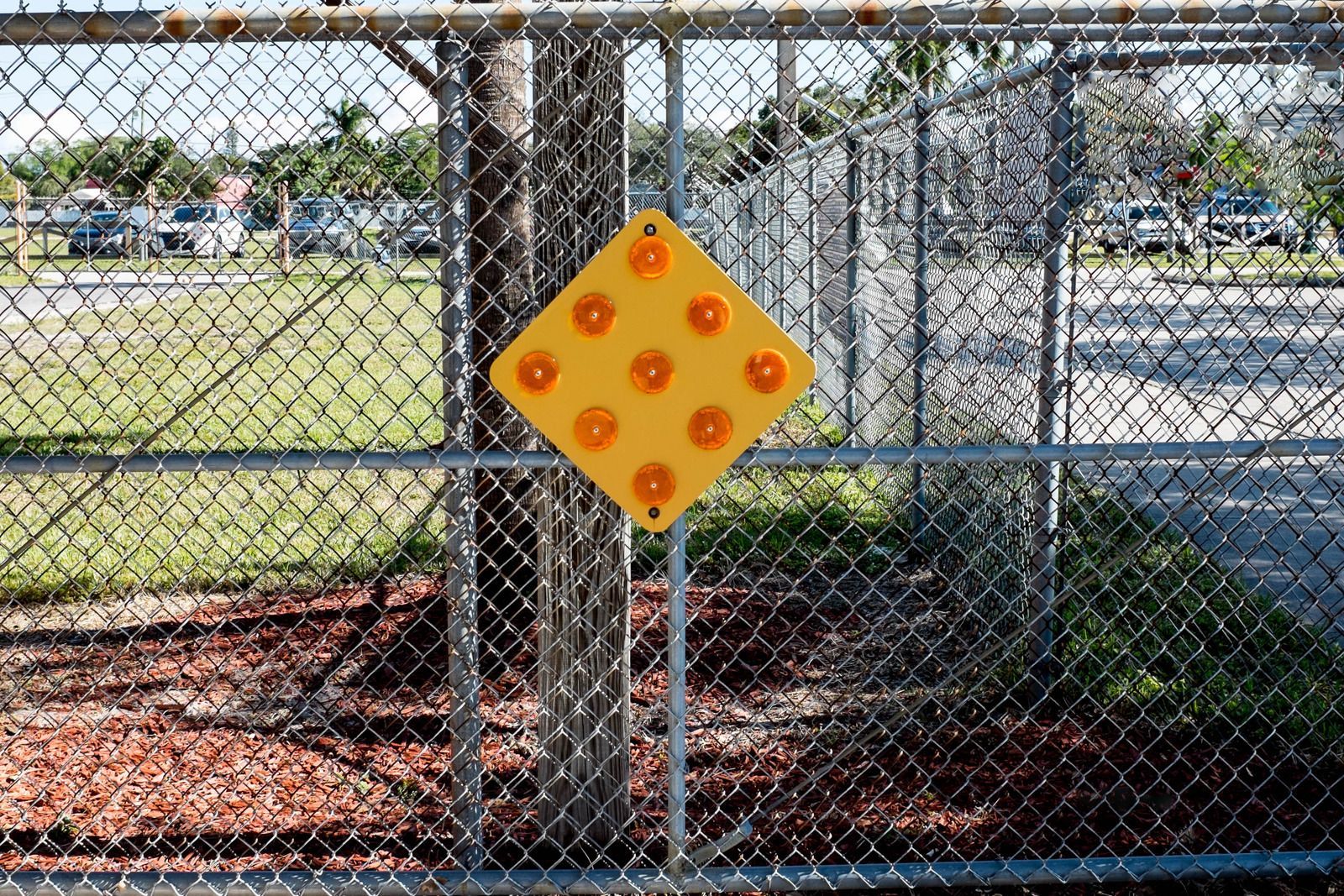 Yellow flashing light sign on a chain-link fence, likely near a school or construction zone.