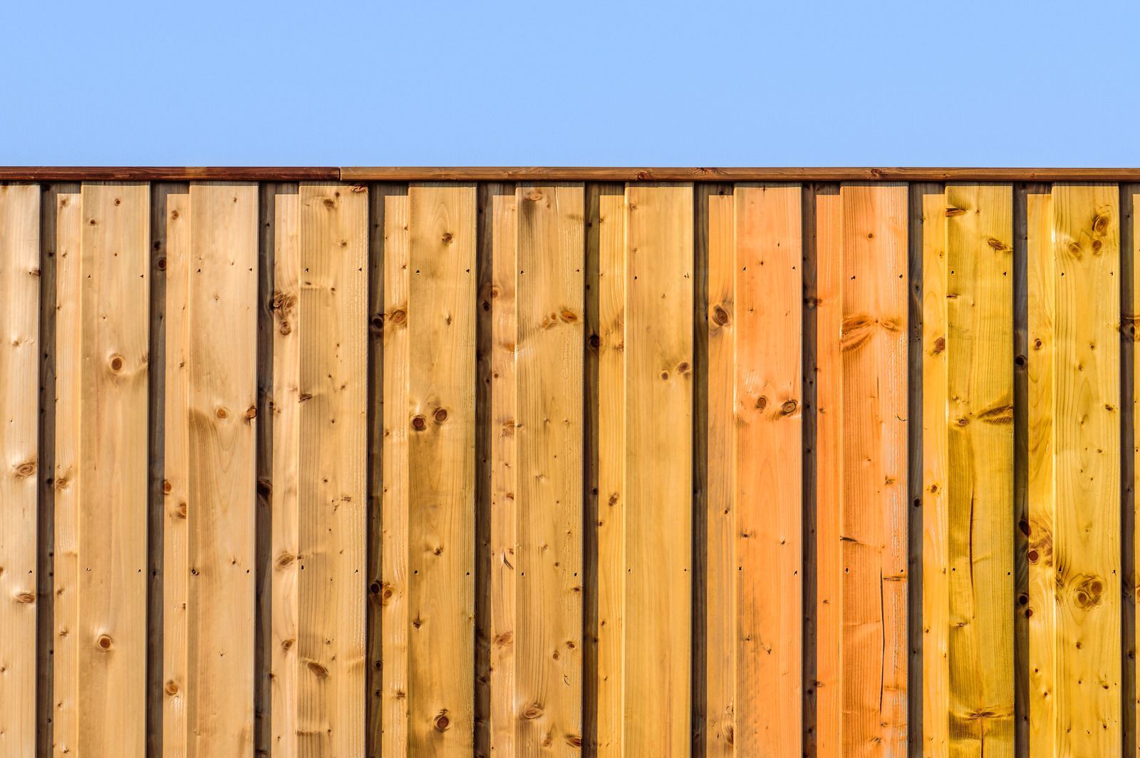 Vertical wooden fence with varying shades of brown and a clear blue sky background.
