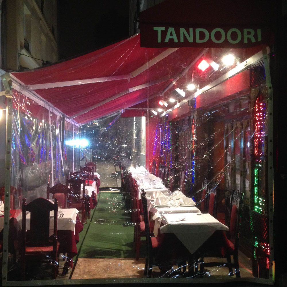 Un restaurant avec des tables et des chaises sous un auvent sur lequel est écrit tandoori