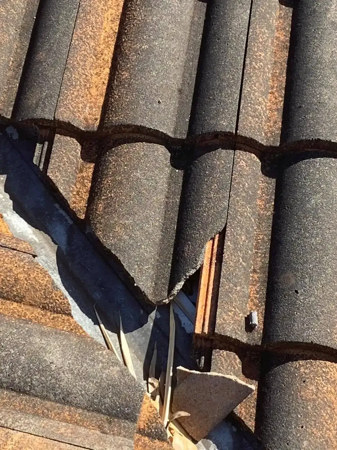 Close-up of a damaged roof with broken dark brown tiles near a gutter. — SEQ Roofing & Painting in Coolangatta, QLD