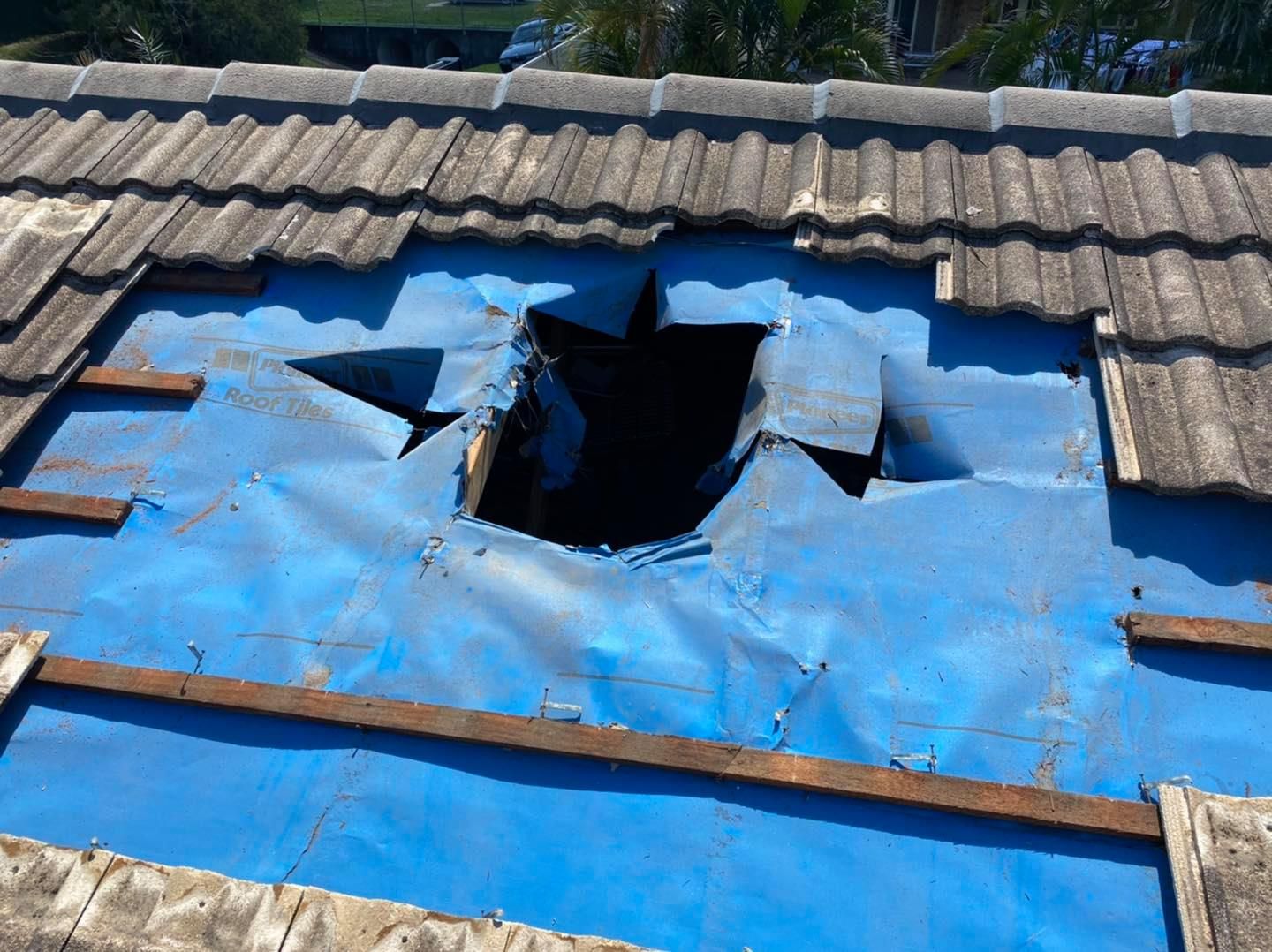 Damaged roof with hole exposing blue underlayment; gray tiles missing. — SEQ Roofing & Painting in Surfers Paradise, QLD