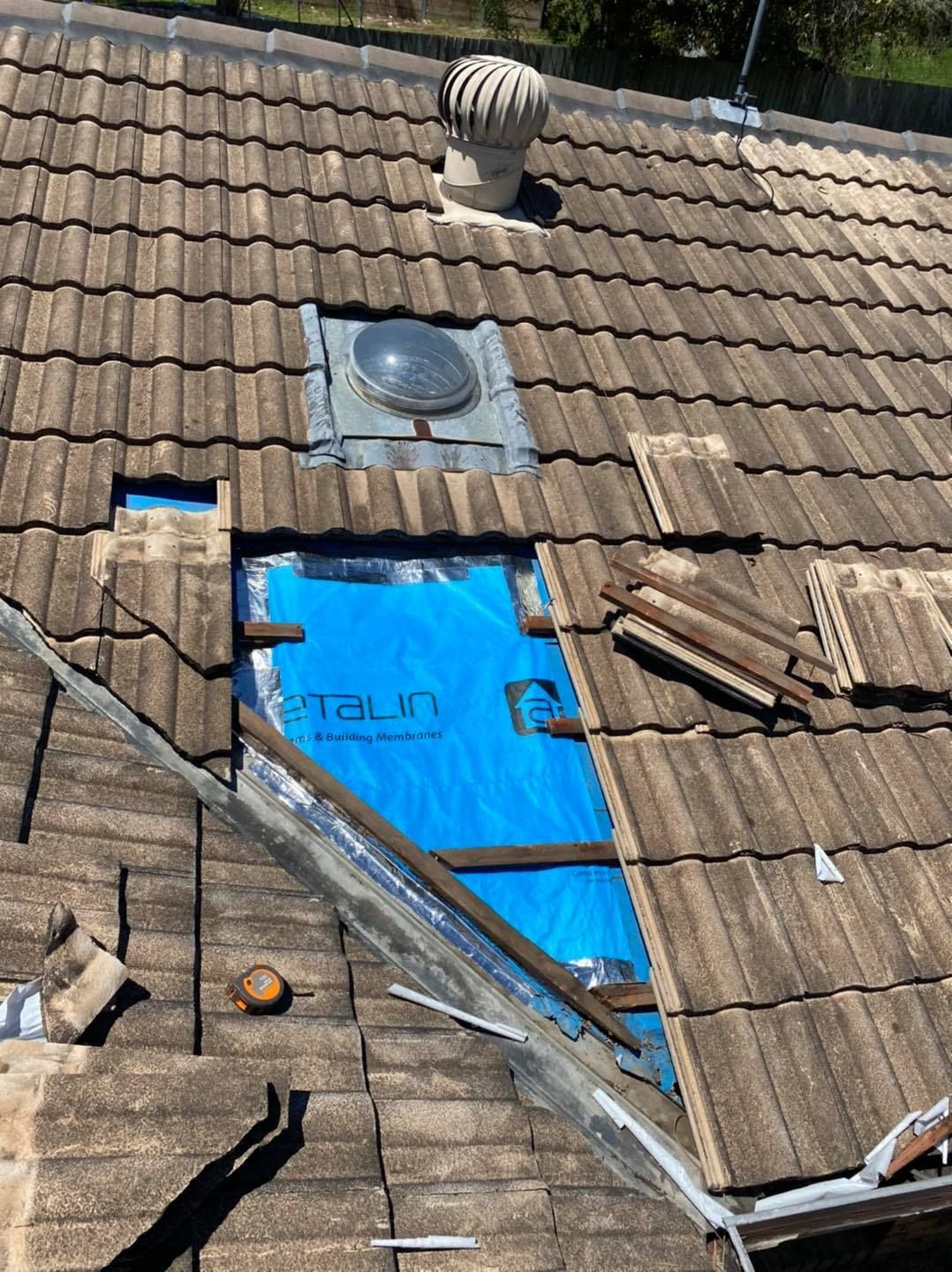 Rooftop with missing tiles, blue tarp covering an opening, and a skylight. — SEQ Roof Repaints In Ipswich, QLD