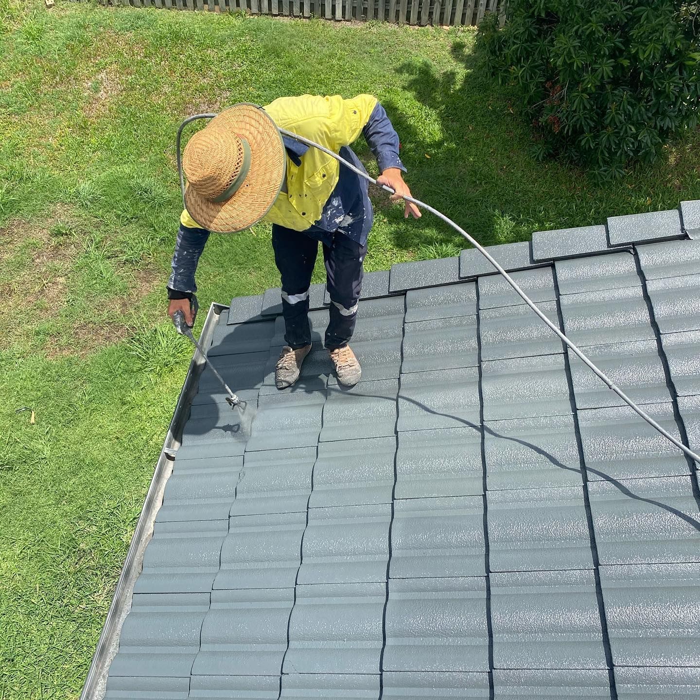 Person Painting a Gray Tiled Roof With a Sprayer, Outdoors on a Sunny Day — SEQ Roofing & Painting in Carrara, QLD