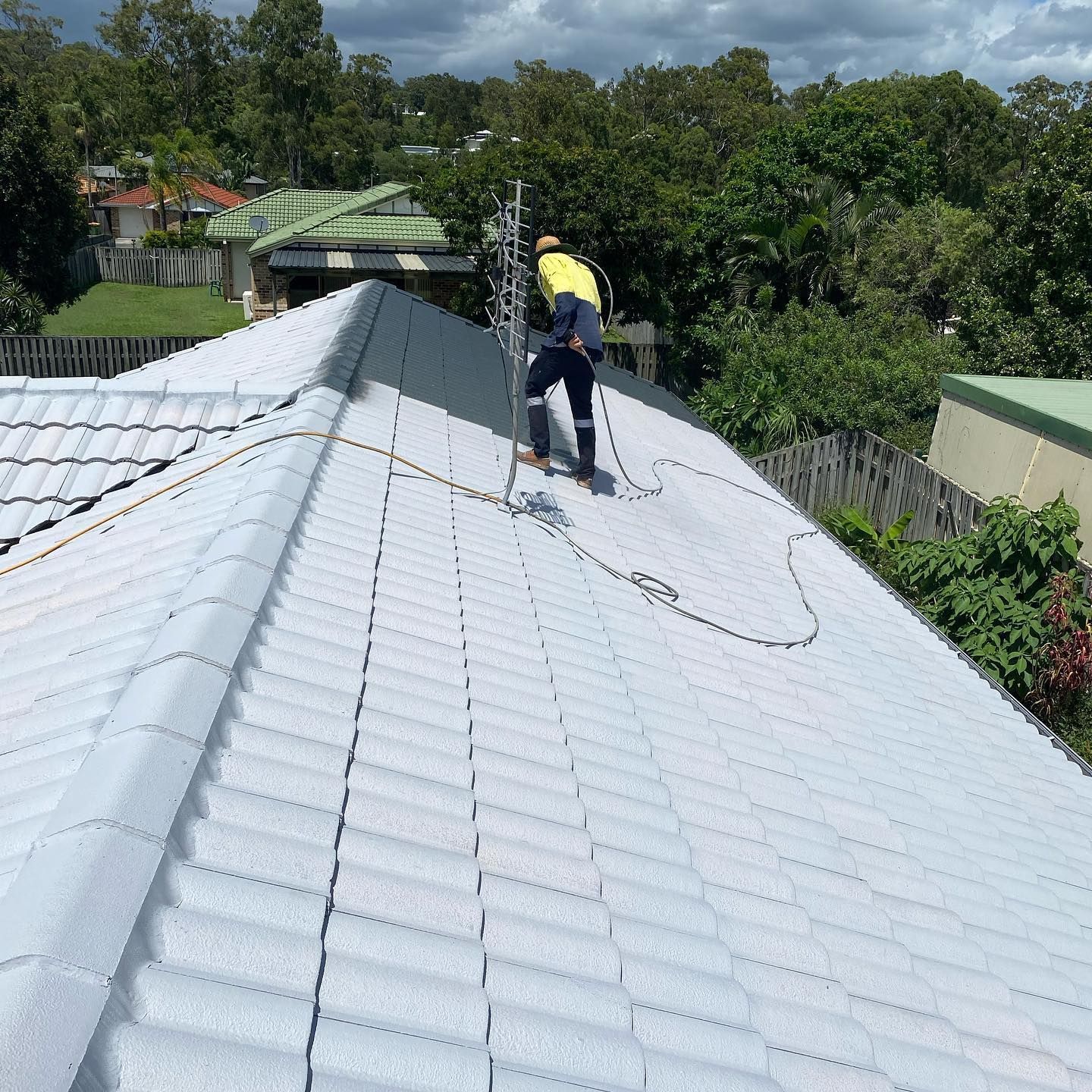 Person on a Roof Painting Tiles, Ladder, Hose, and Houses in Background — SEQ Roofing & Painting in Tugun, QLD