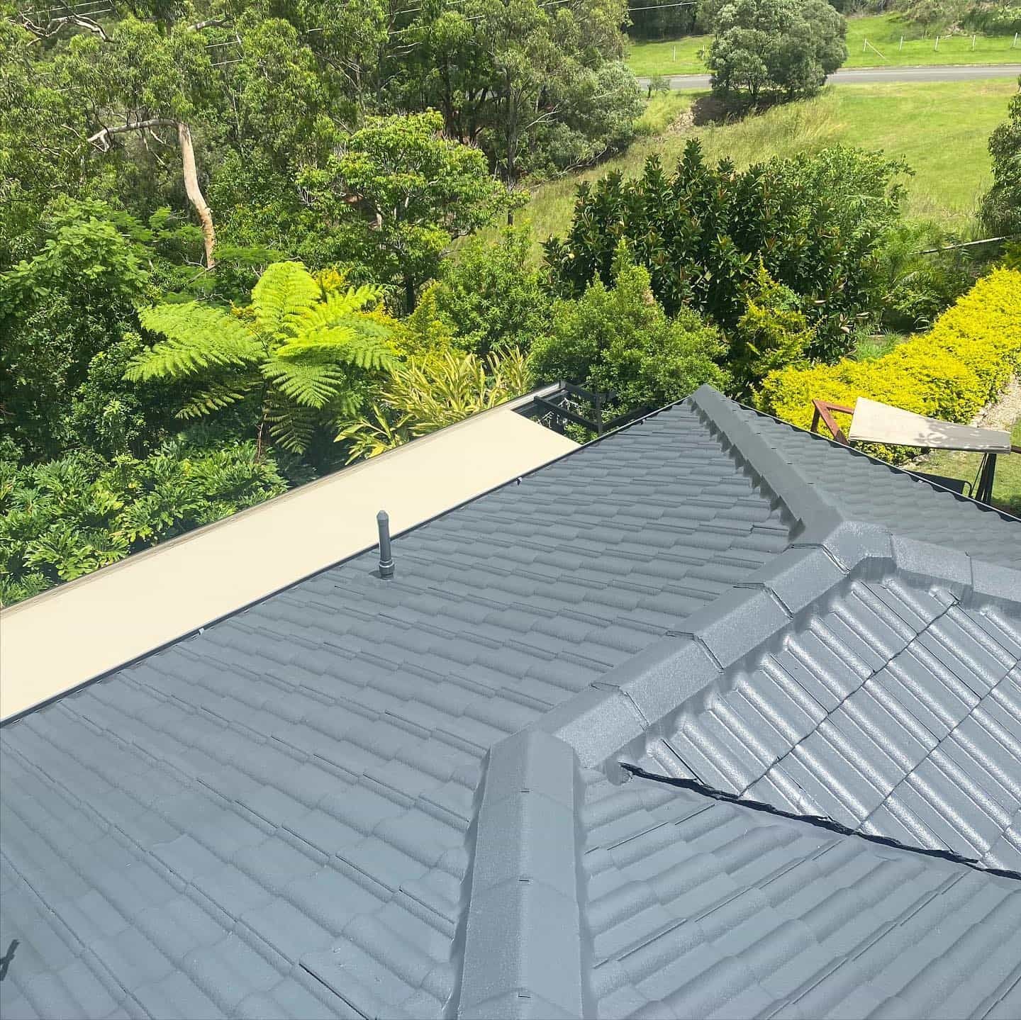 Grey metal roof with angled ridges, set against green trees and a sunny sky. — SEQ Roof Repaints In Jimboomba, QLD