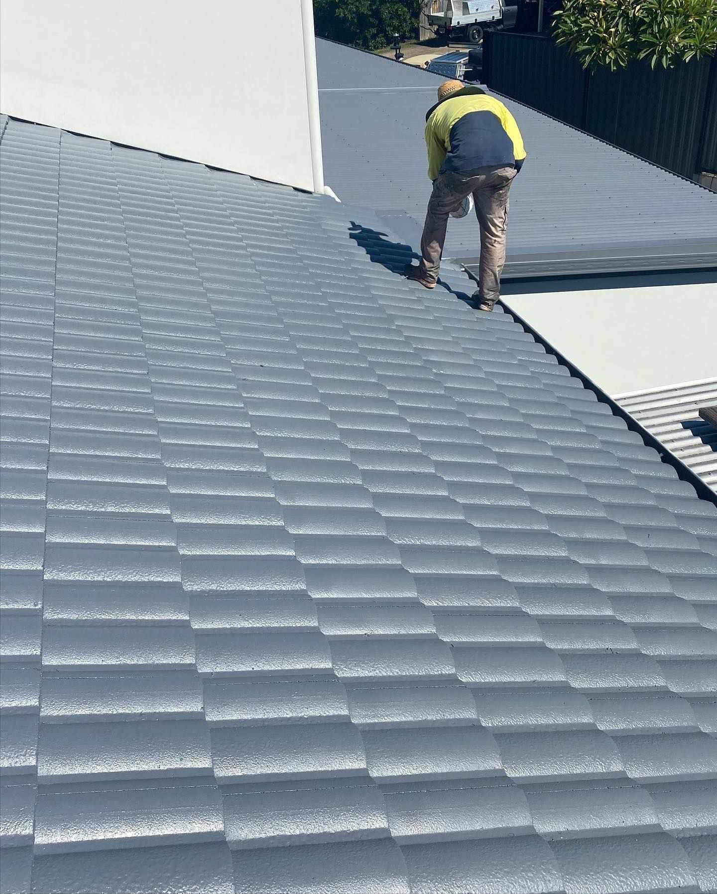 Person Working on a Gray Tile Roof, Wearing Work Clothes — SEQ Roofing & Painting in Coolangatta, QLD