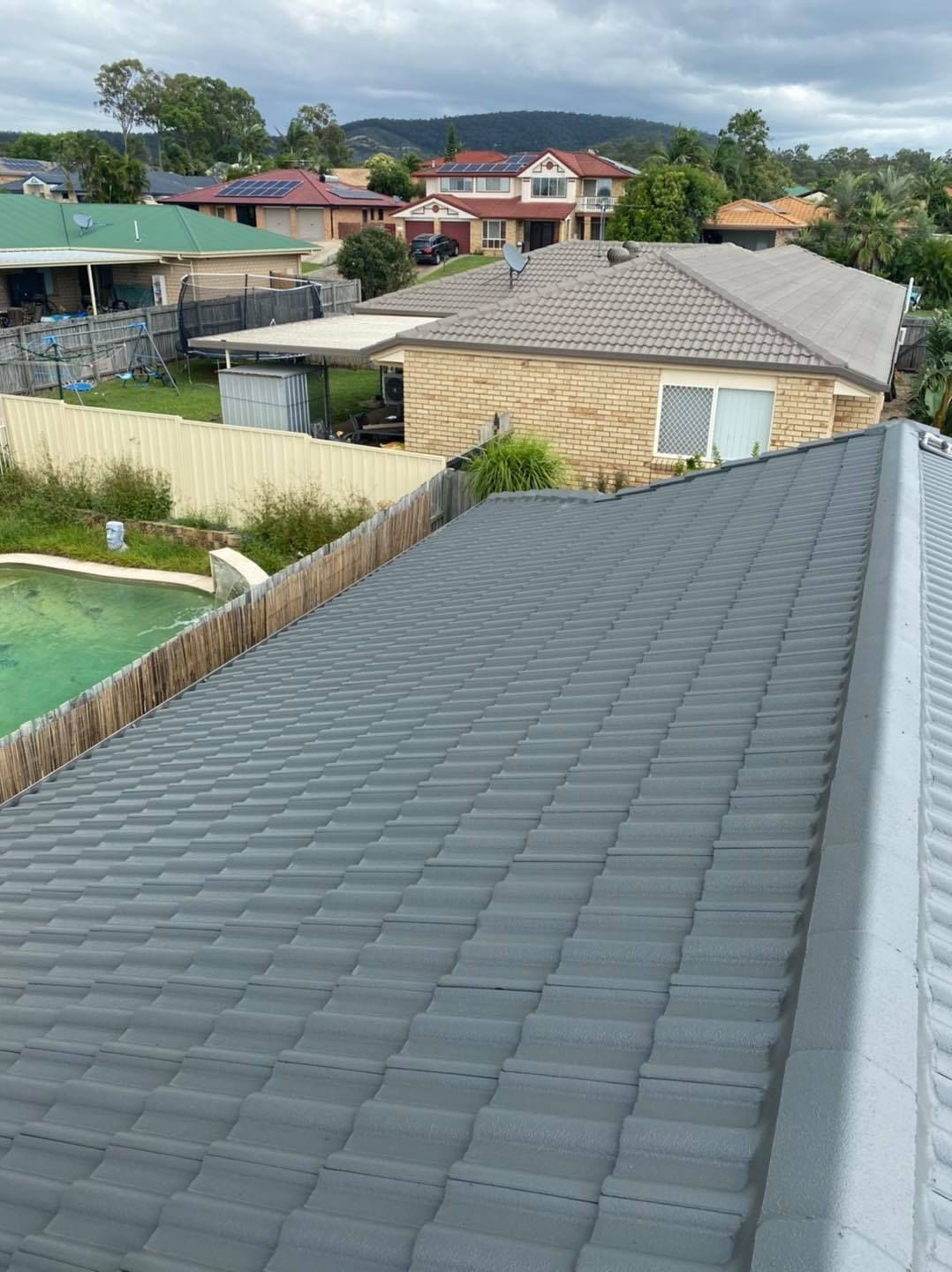 Gray tiled roof of a house overlooking other houses in a suburban area on a cloudy day. — SEQ Roof Repaints In Ipswich, QLD