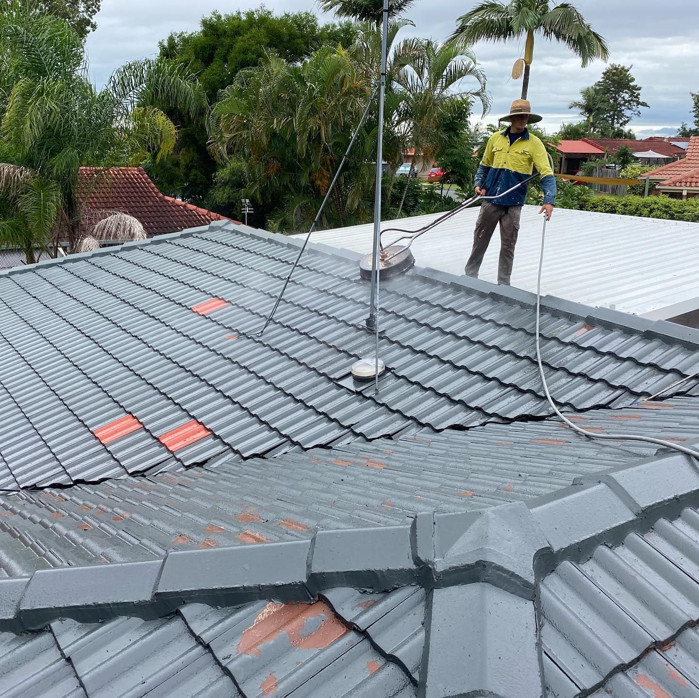 Man Power Washes a Gray Tiled Roof — SEQ Roof Repaints In Logan, QLD
