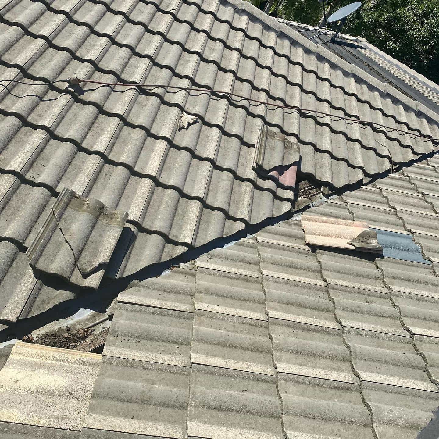 Damaged gray tiled roof with missing and broken tiles, showing a section in need of repair. — SEQ Roof Repaints In Bonogin, QLD
