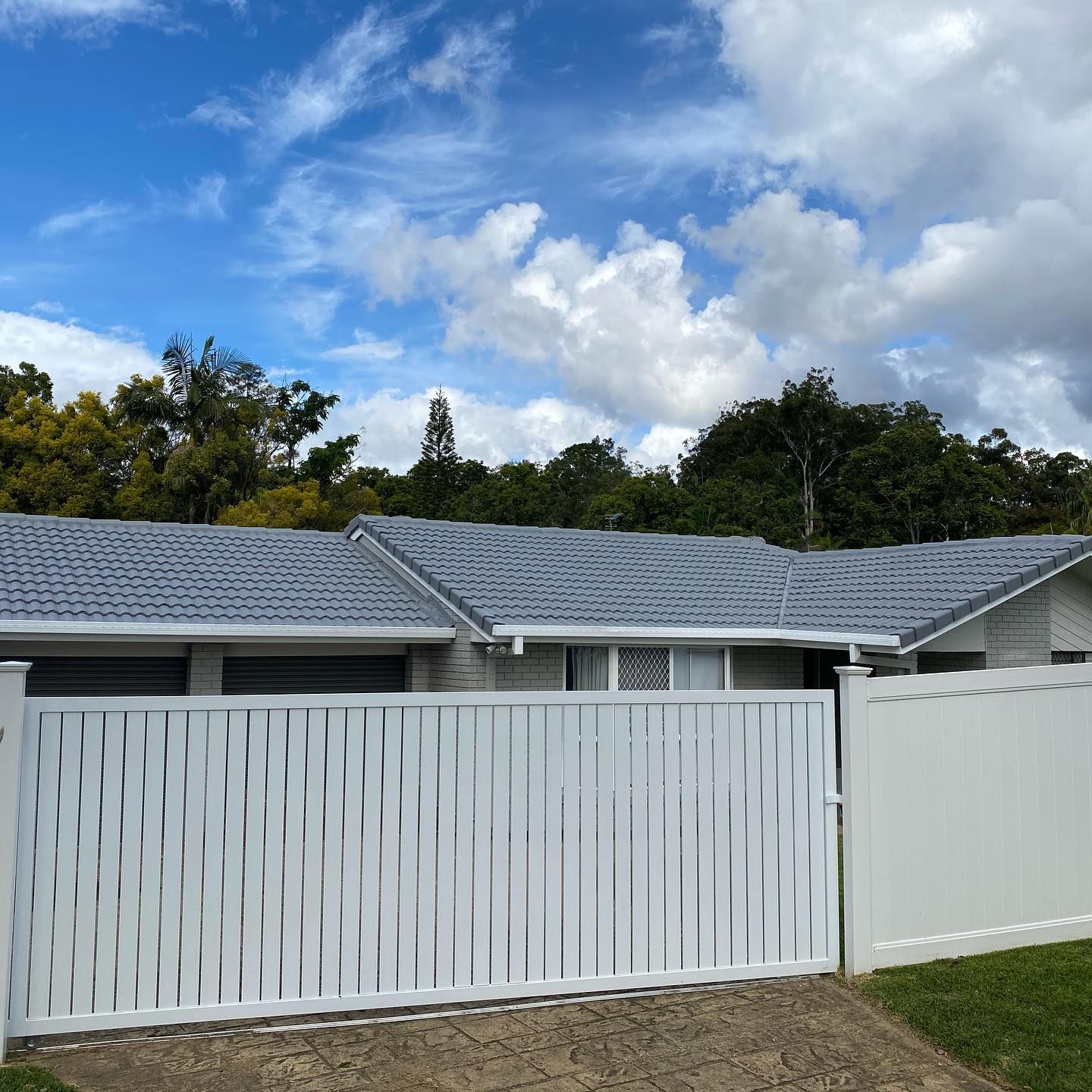 White Fenced House with Blue Roof Under Cloudy Sky — SEQ Roof Repaints In Ipswich, QLD