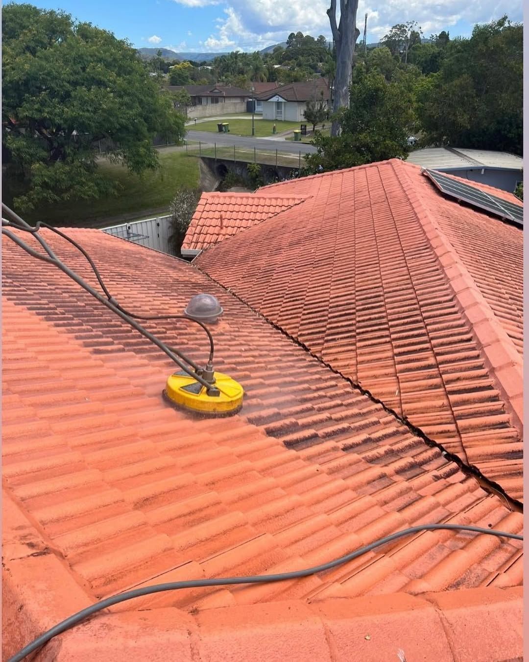 A person pressure washing a terracotta tile roof on a sunny day. — SEQ Roof Repaints In Jimboomba, QLD
