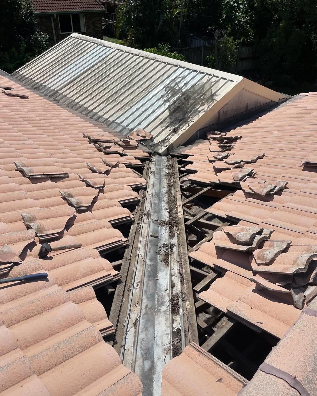 Damaged terracotta tile roof with a deteriorated metal valley; sunlight. — SEQ Roof Repaints In Jimboomba, QLD