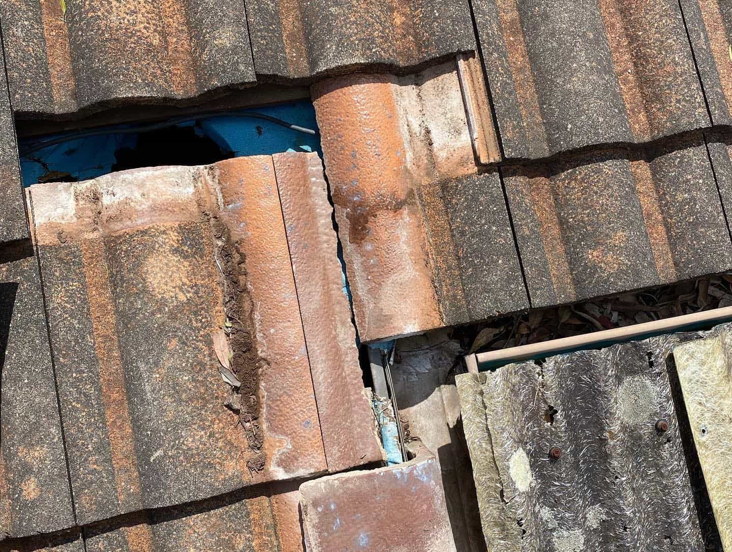 Damaged terracotta roof tiles with a hole exposing blue underlayment and a broken pipe. — SEQ Roof Repaints In Tweed Heads, QLD
