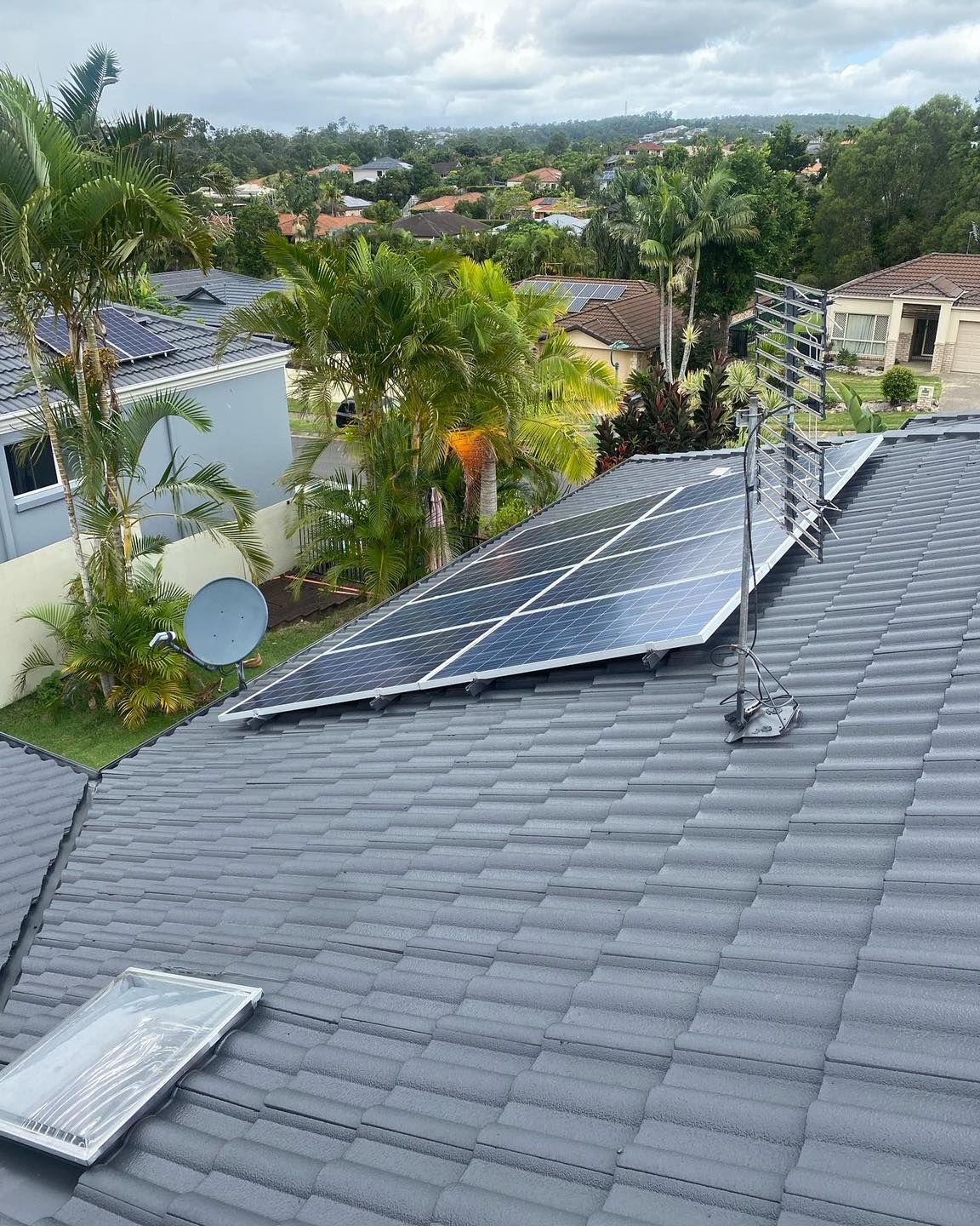 Solar Panels on a Roof Overlooking a Suburban Area With Trees and Houses. Cloudy Sky — SEQ Roofing & Painting in Nerang, QLD
