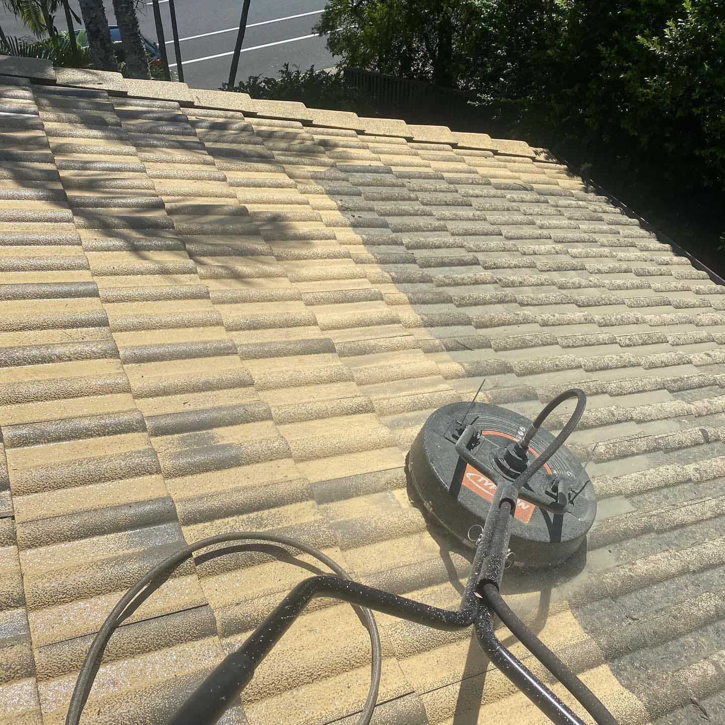 A person power washing a roof with a rotating surface cleaner, showing a strip of clean shingles. — SEQ Roof Repaints In Tweed Heads, QLD