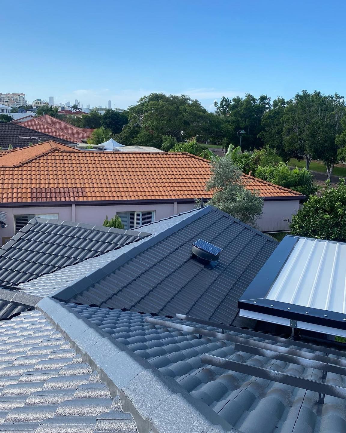 Rooftop view: Dark grey tiled roof with a skylight and metal trim, looking over neighborhood rooftops and trees. — SEQ Roof Repaints In Bonogin, QLD