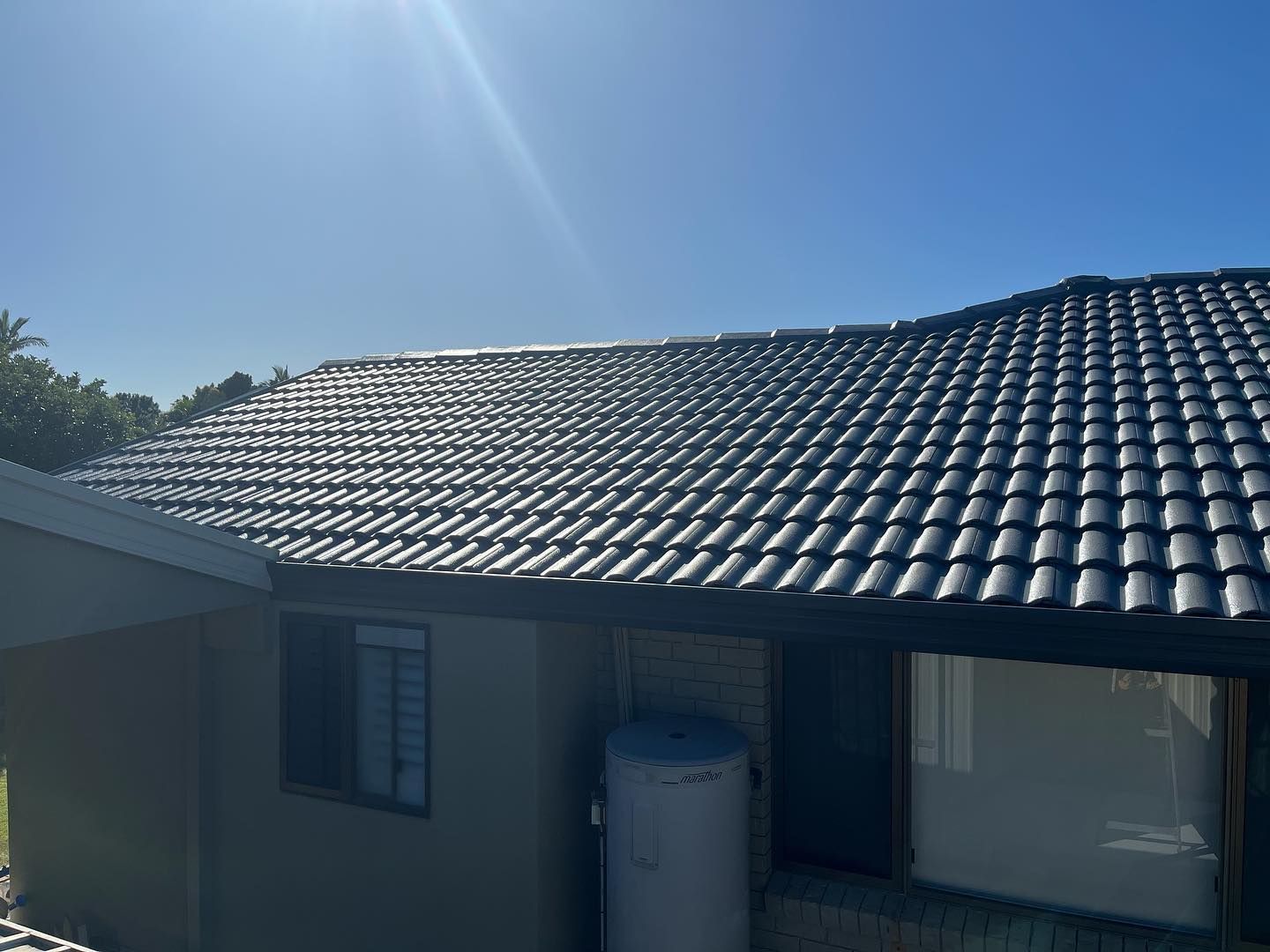 Black Tiled Roof on a House, Under a Bright Blue Sky — SEQ Roofing & Painting in Pacific Pines, QLD