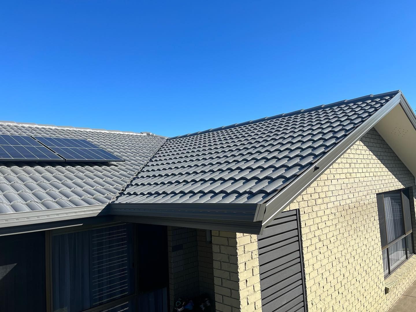 Tiled Roof With Solar Panel Against a Clear Blue Sky, Light Brick House Exterior — SEQ Roofing & Painting in Hope Island, QLD
