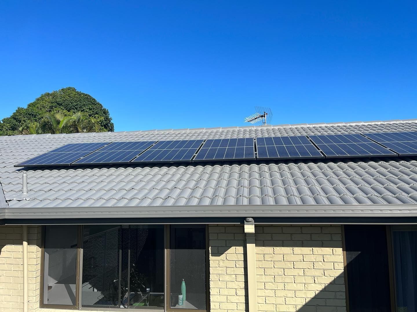Solar Panels on A Gray Tiled Roof Against a Bright Blue Sky — SEQ Roof Repaints In Ipswich, QLD