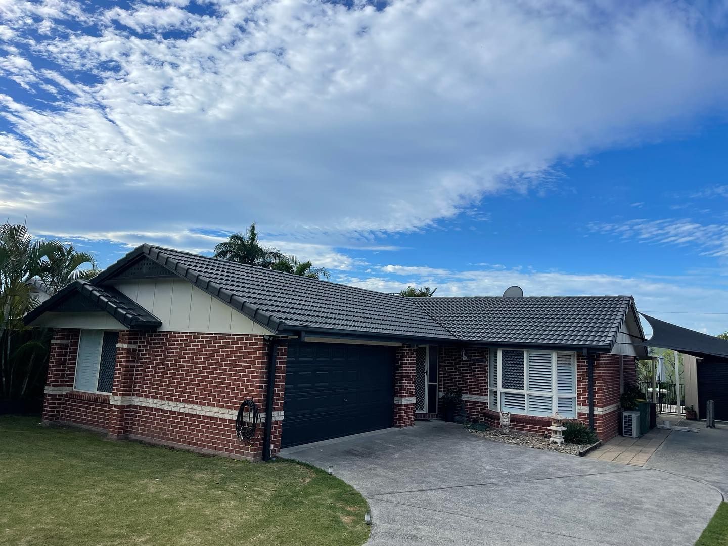 Brick Home With Dark Roof, Garage, Driveway, and Blue Sky With Clouds — SEQ Roofing & Painting in Hope Island, QLD