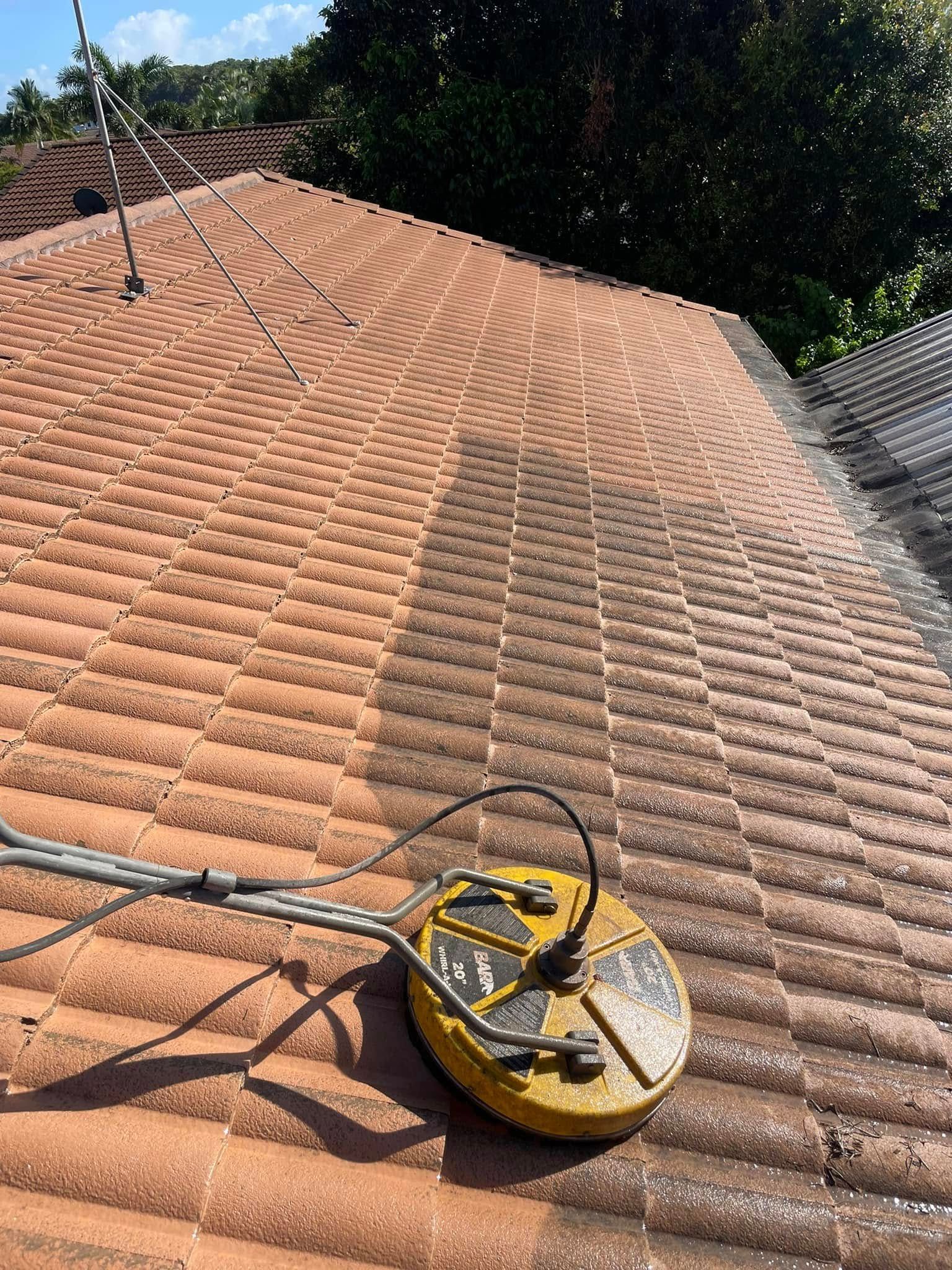 A Yellow Pressure Washing Machine on a Red Tile Roof, Cleaning a Strip of the Roof — SEQ Roofing & Painting in Labrador, QLD