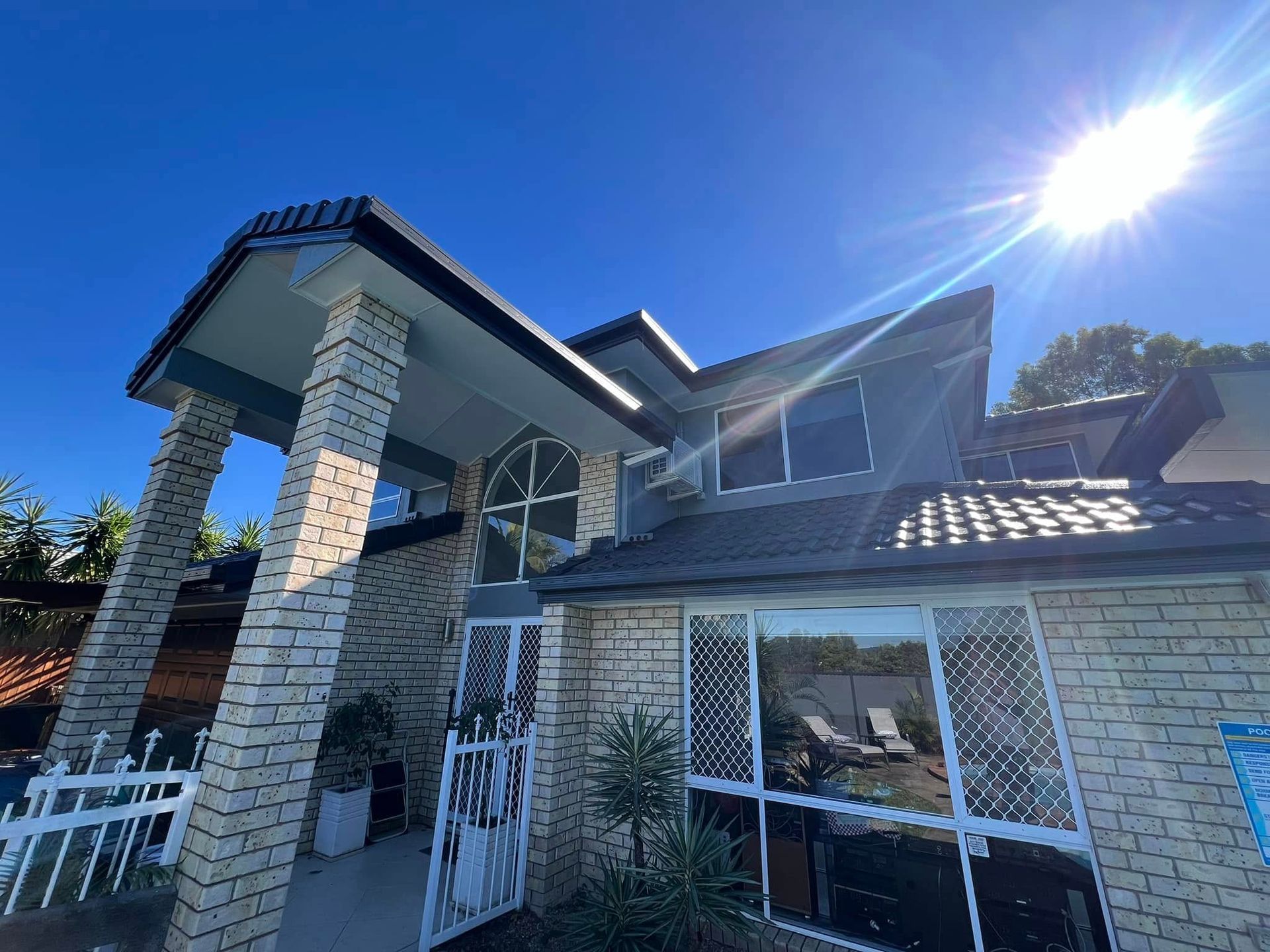 House With Brick Columns, Gray Roof, and Arched Window Under a Bright Sun — SEQ Roofing & Painting in Carrara, QLD