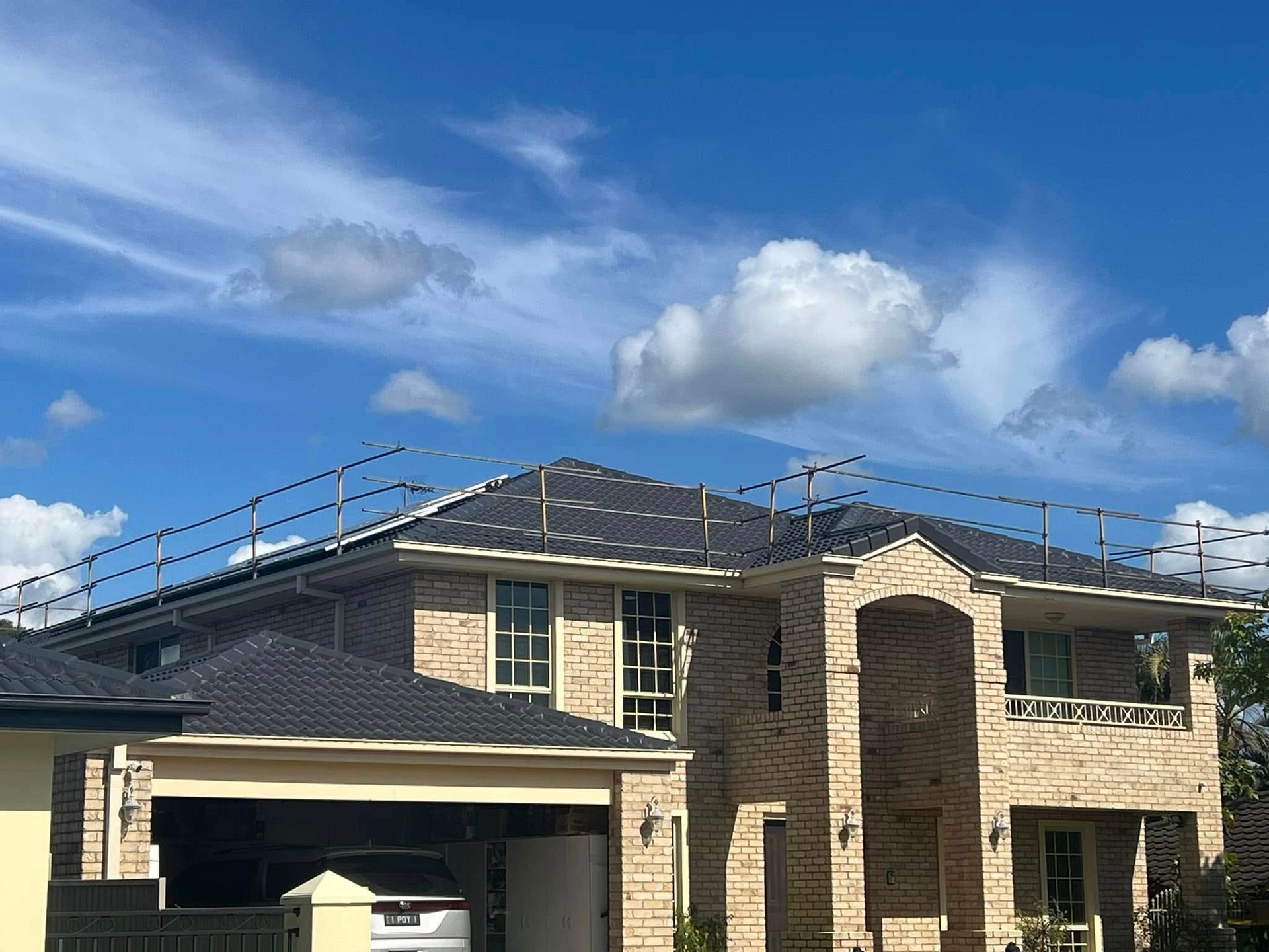 Large Brick House With Dark Roof Tiles, Safety Railing, and Blue Sky — SEQ Roofing & Painting in Tugun, QLD