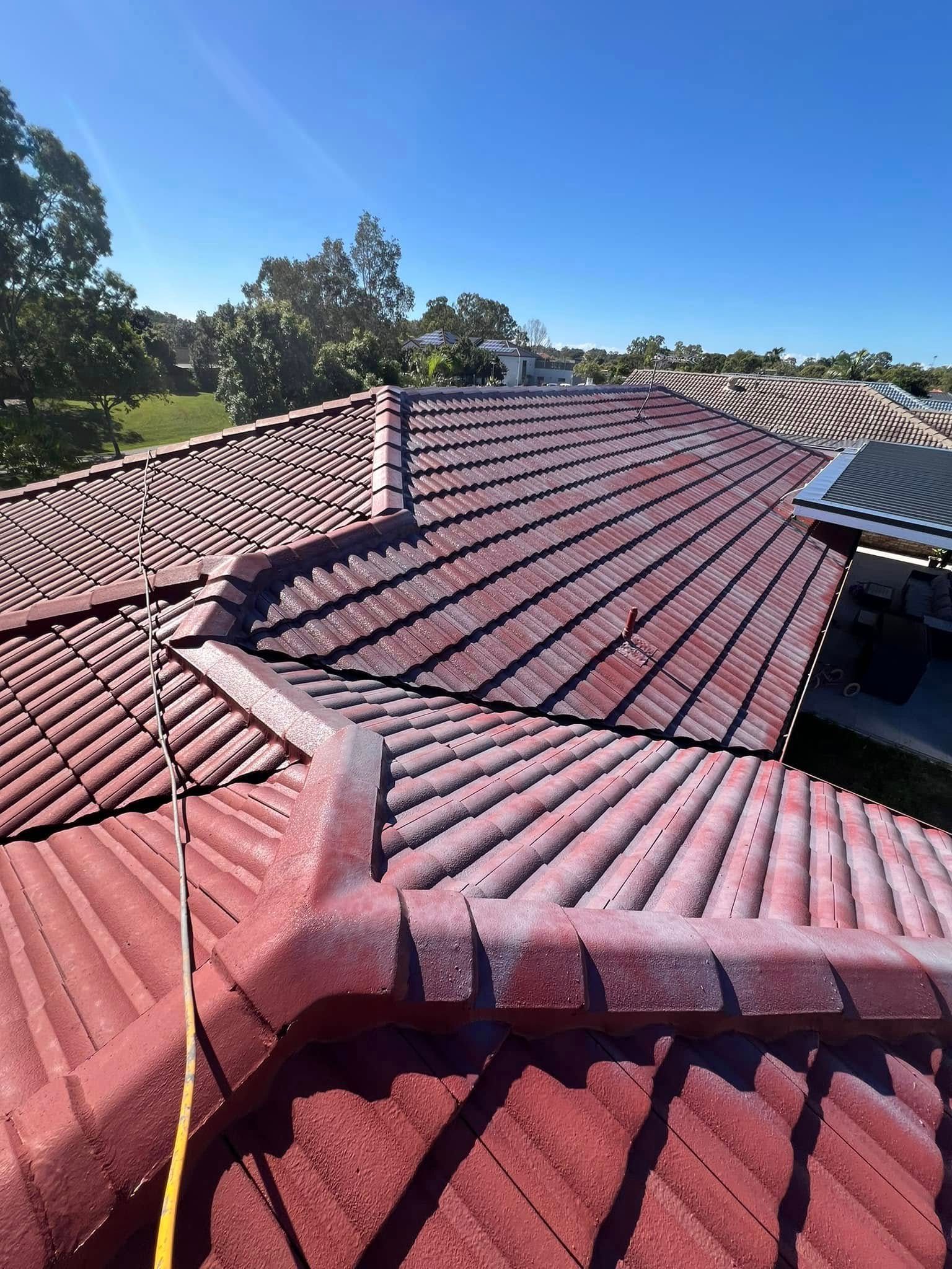 Red tiled roof on a sunny day with visible ridge capping and surrounding trees. — SEQ Roofing & Painting in Isle of Capri, QLD