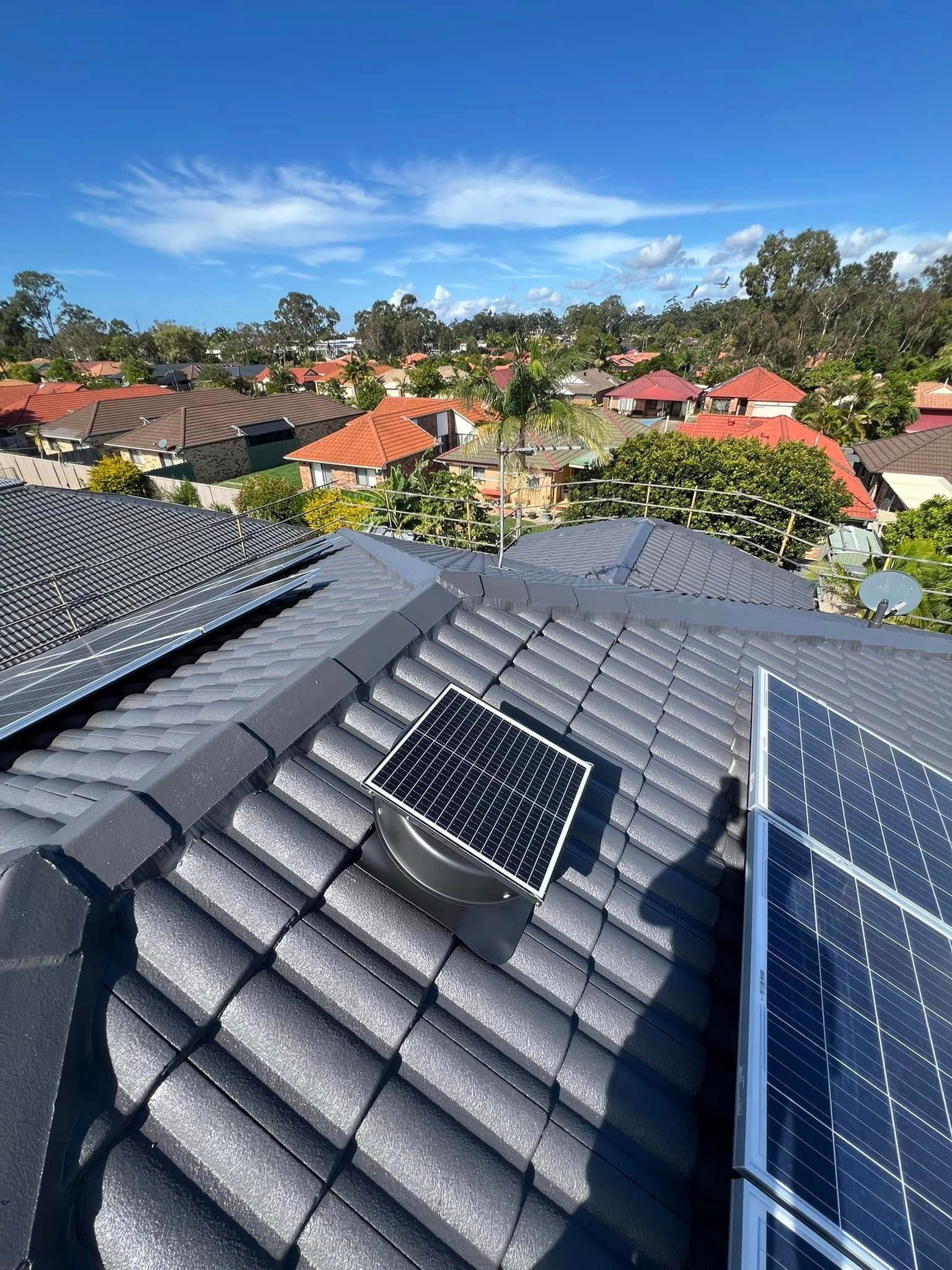 Solar Roof Vent Between Solar Panels on A Tiled Roof, Residential Area Backdrop — SEQ Roof Repaints In Bonogin, QLD