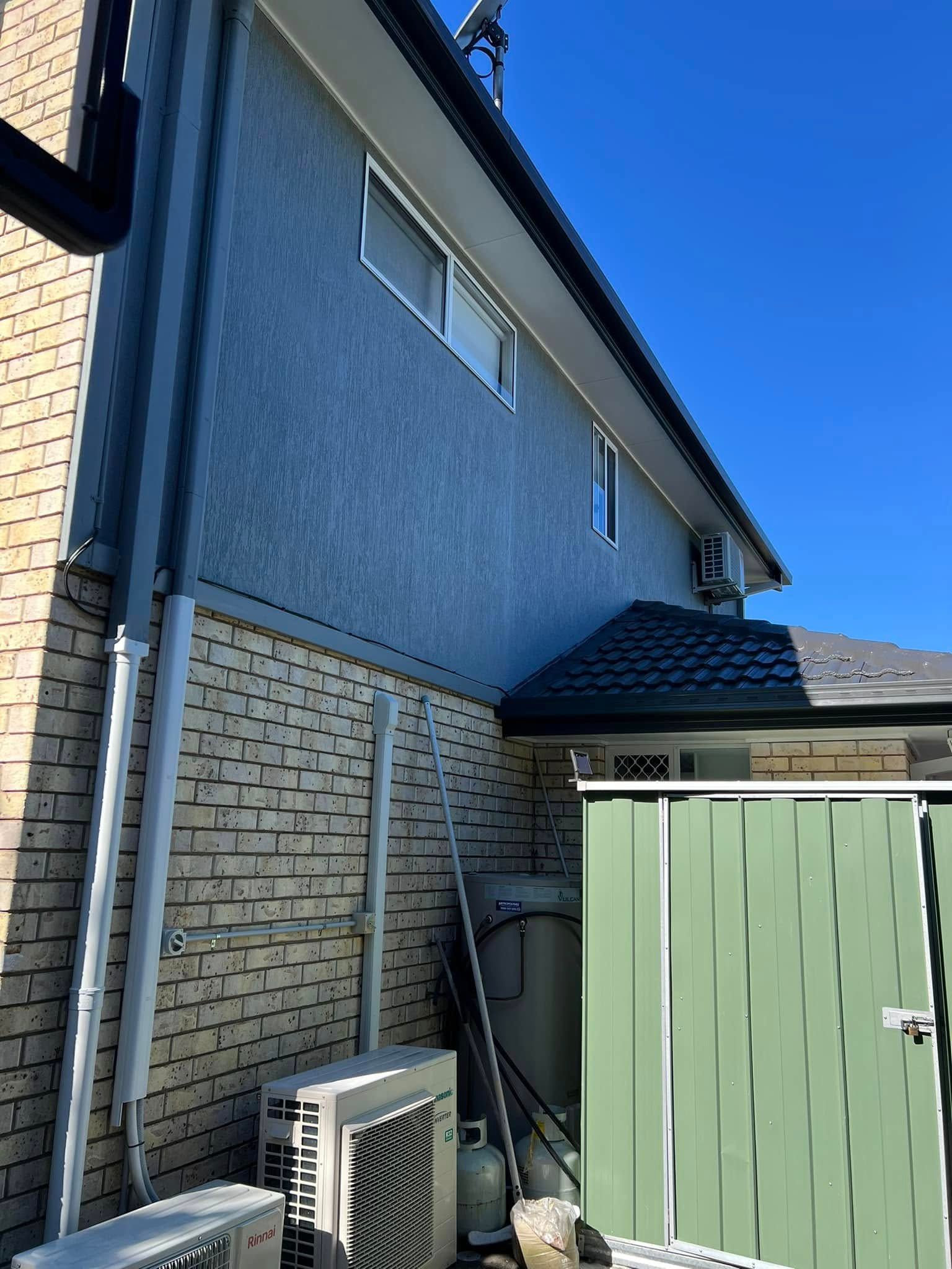 Blue House With Brick Base and Green Fence on a Sunny Day — SEQ Roofing & Painting in Currumbin, QLD