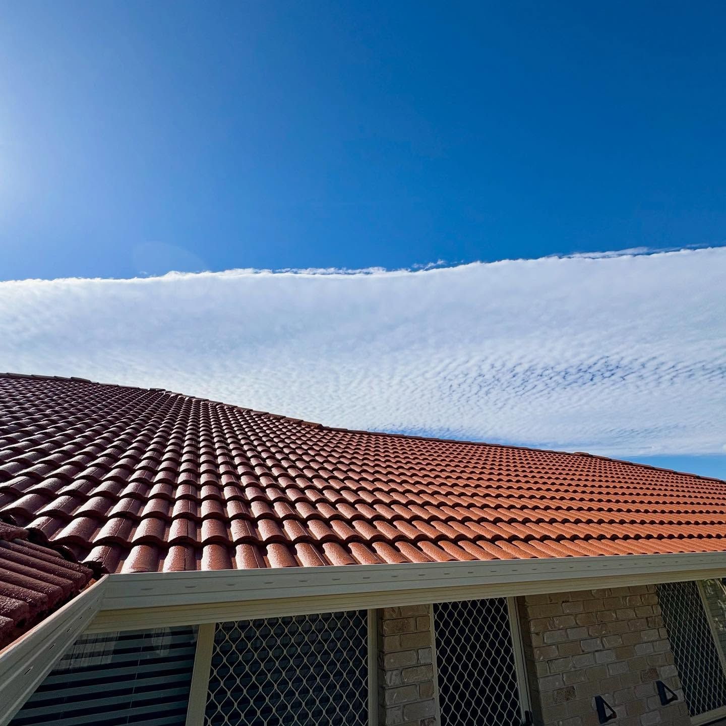 Red Tiled Roof Under a Bright Blue Sky With a Long White Cloud — SEQ Roofing & Painting in Nerang, QLD