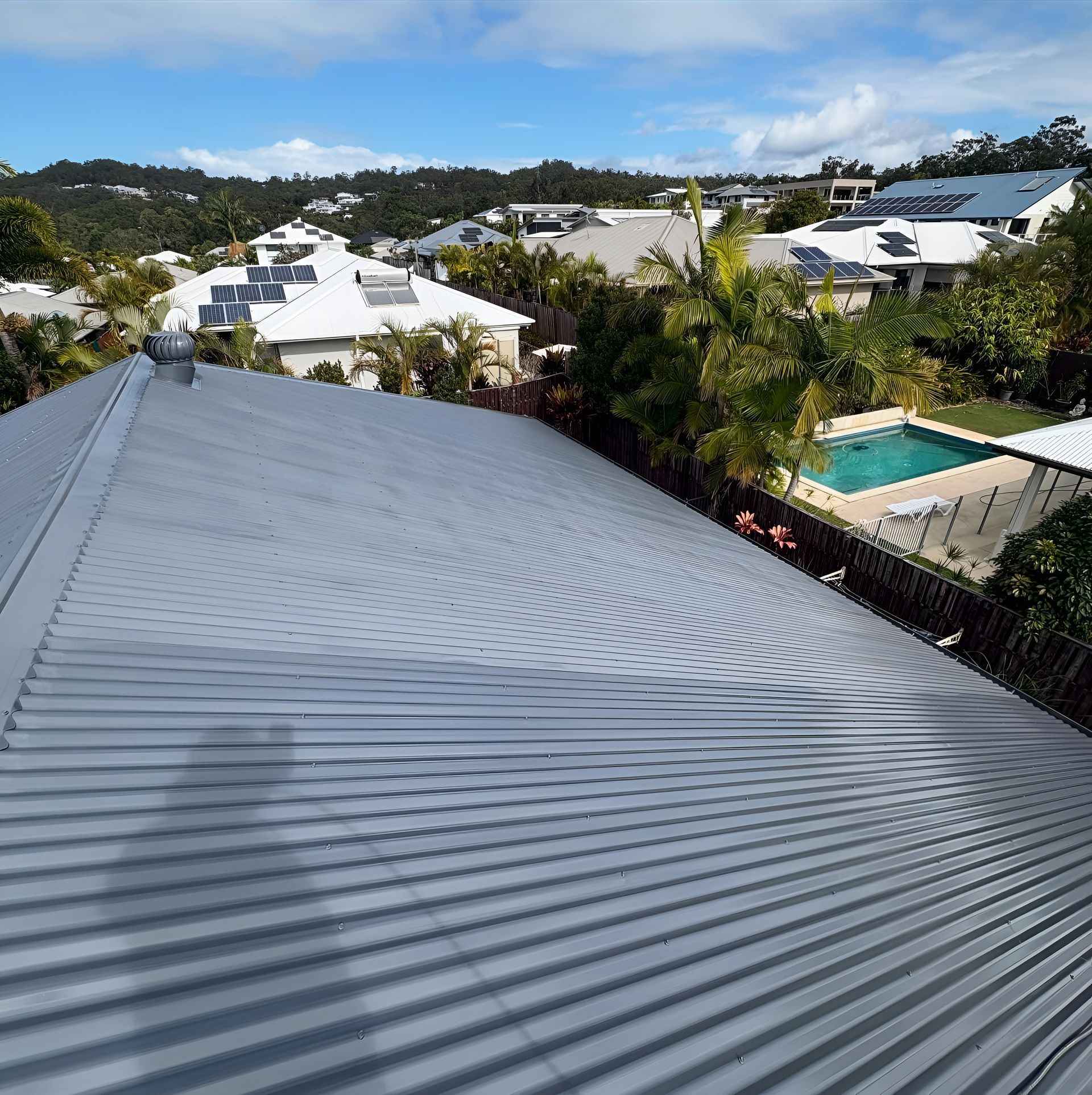 Gray Corrugated Metal Roof with Houses and A Pool — SEQ Roof Repaints In Bonogin, QLD