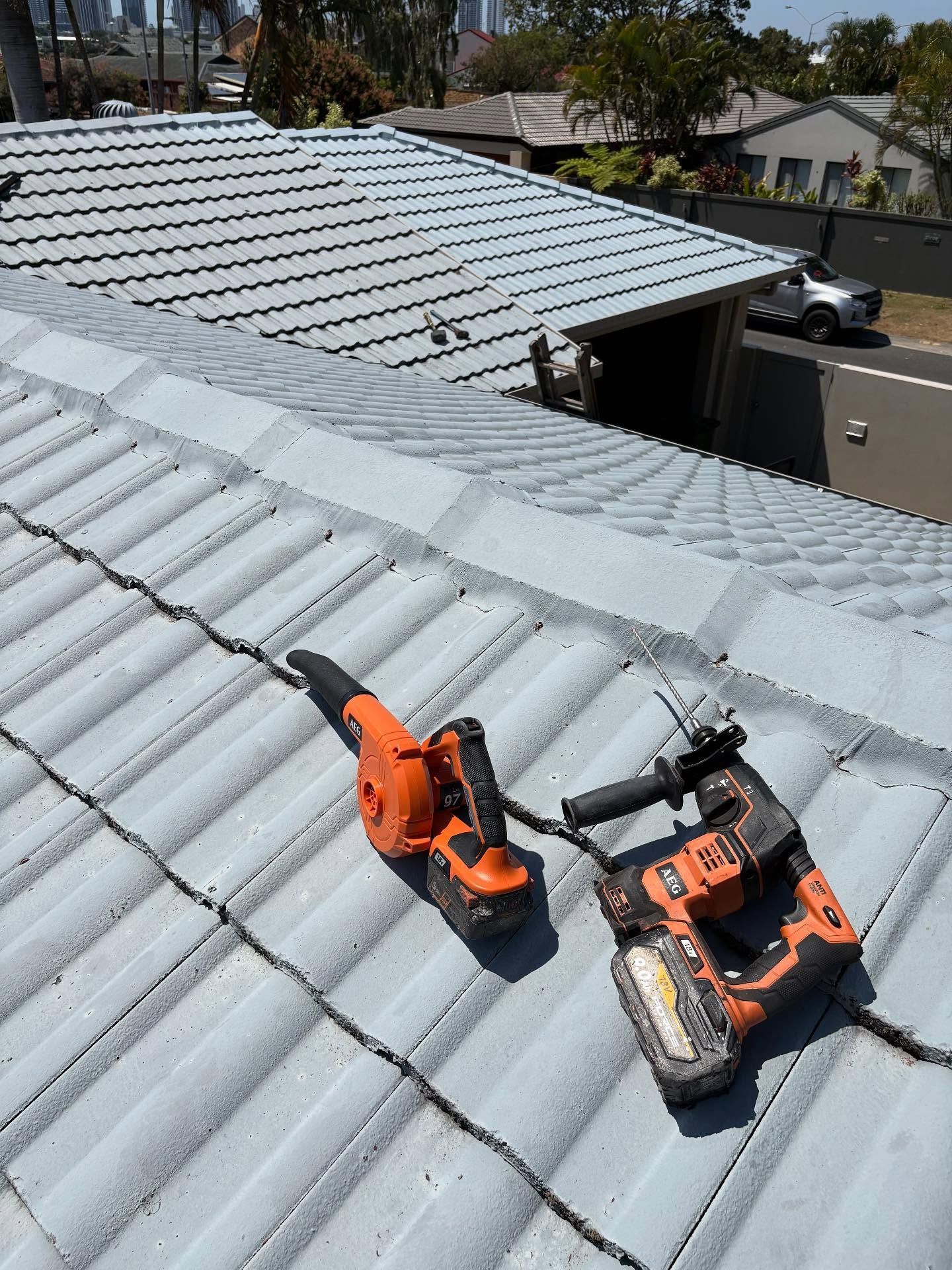 An Orange Blower and Black Drill Lie on a Gray Tile Roof. Sunny Outdoor Setting — SEQ Roofing & Painting in Hope Island, QLD