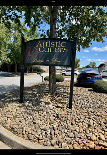 Hair salon interior with brown door, TV, chair, sink, gold clock, and textured walls.