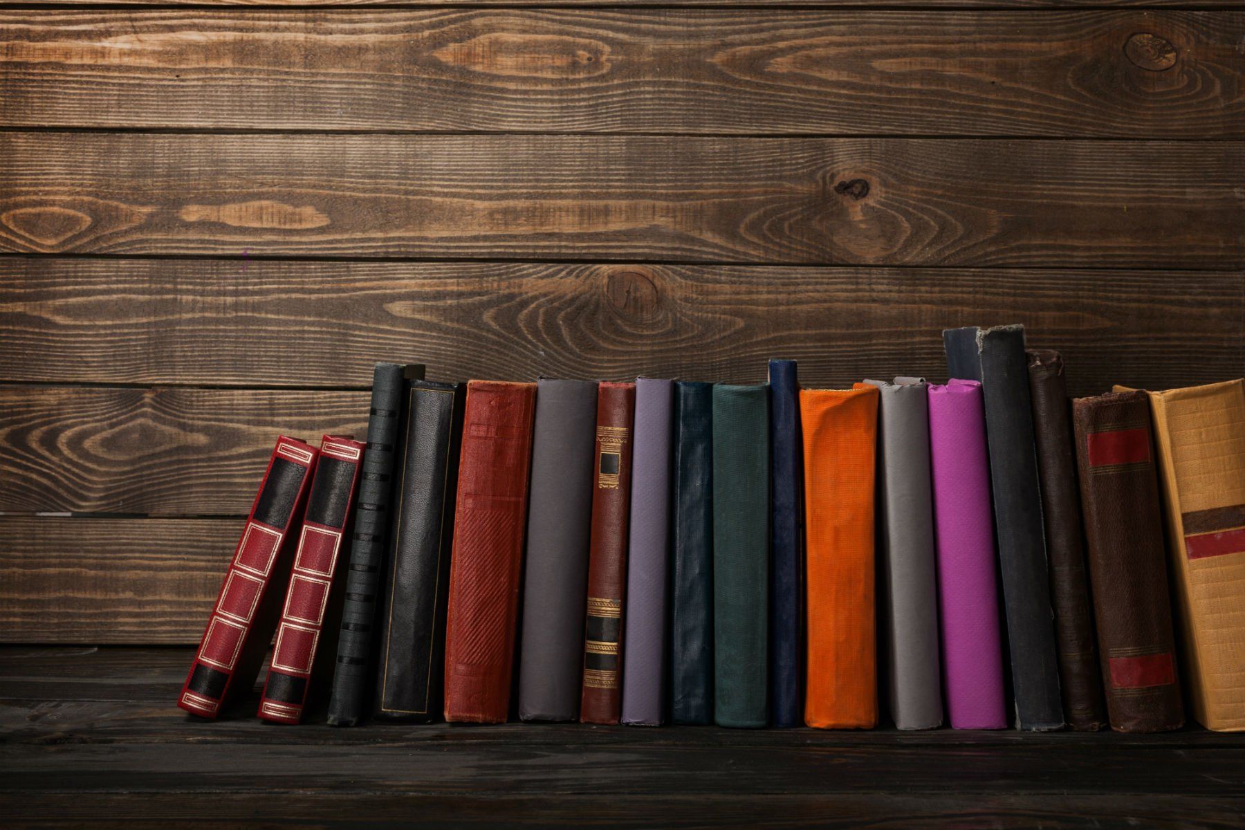 Una fila di libri appoggiati su uno scaffale di legno.