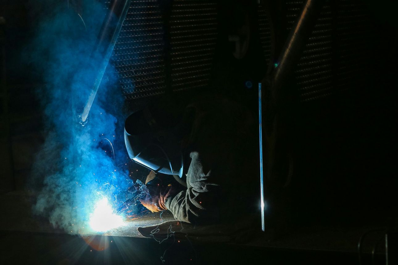 Welder working, sparks and bright blue light illuminating the dark workshop.