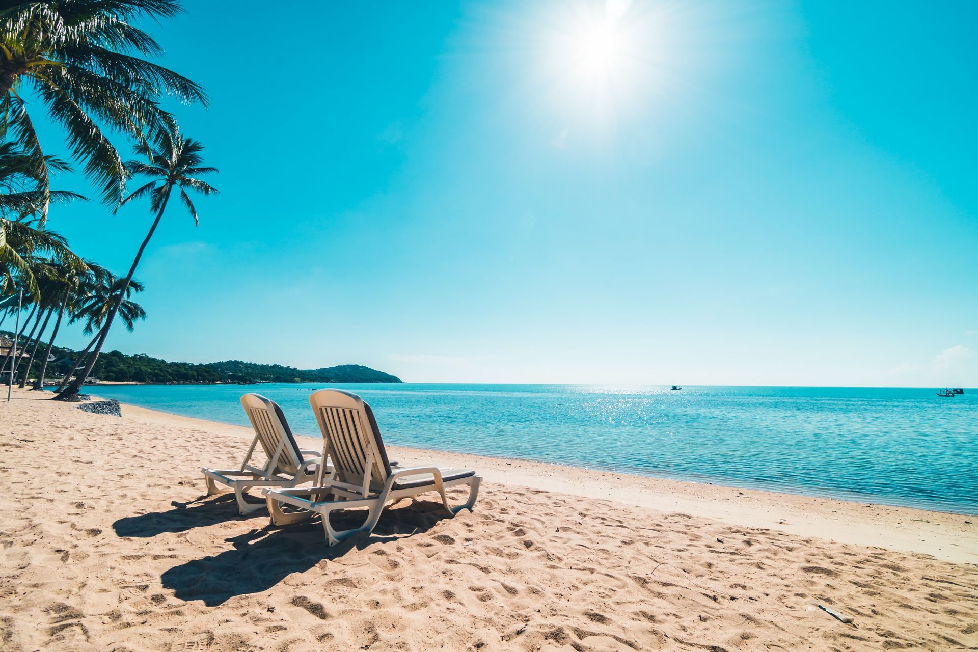 Two lounge chairs are sitting on a sandy beach near the ocean.