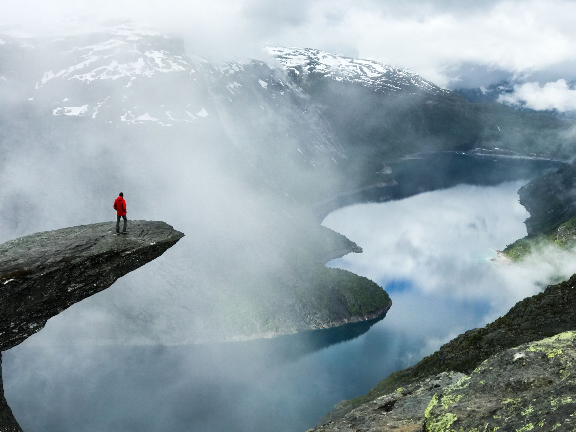 A man is standing on the edge of a cliff overlooking a lake.