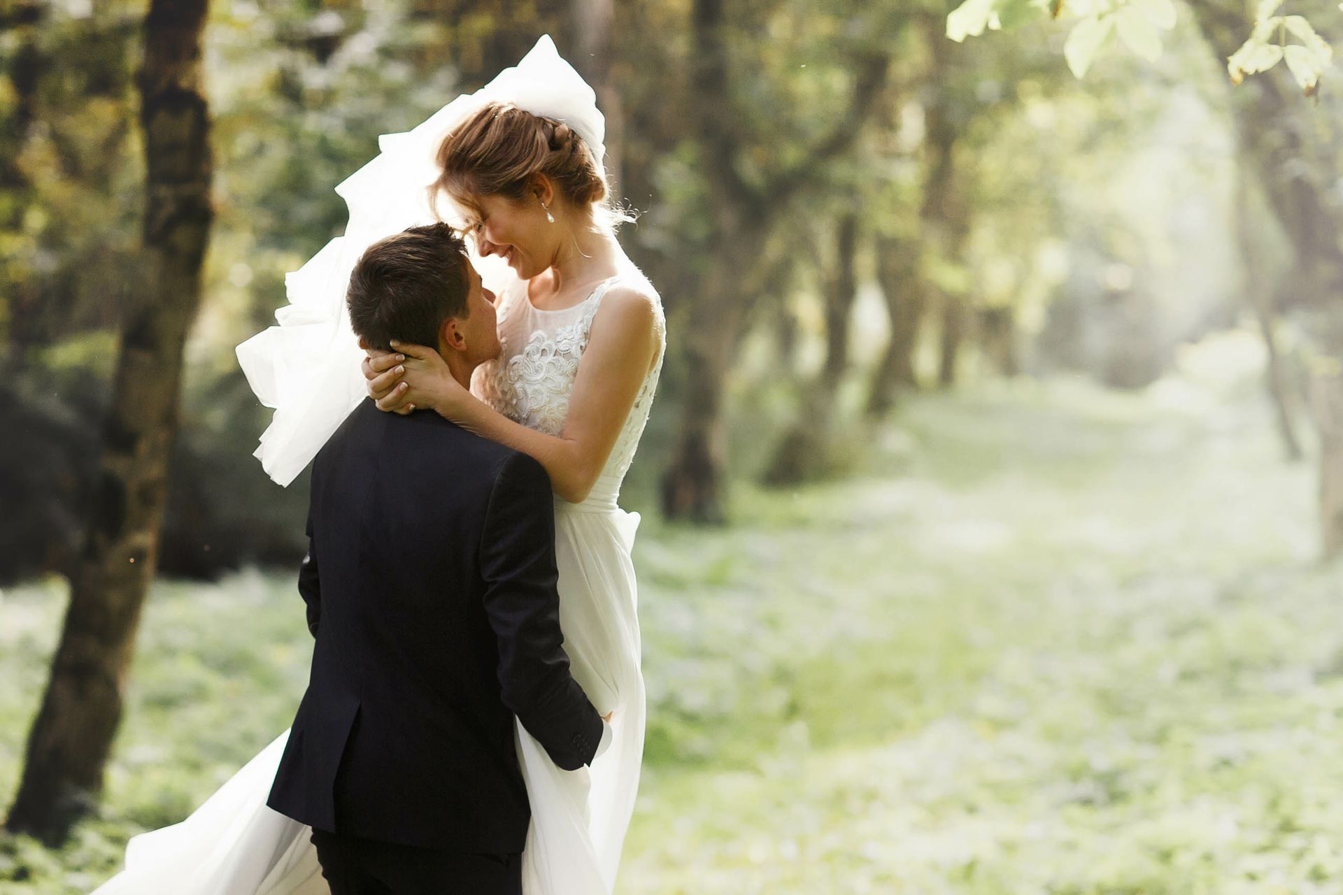 A bride and groom are kissing in the woods on their wedding day.